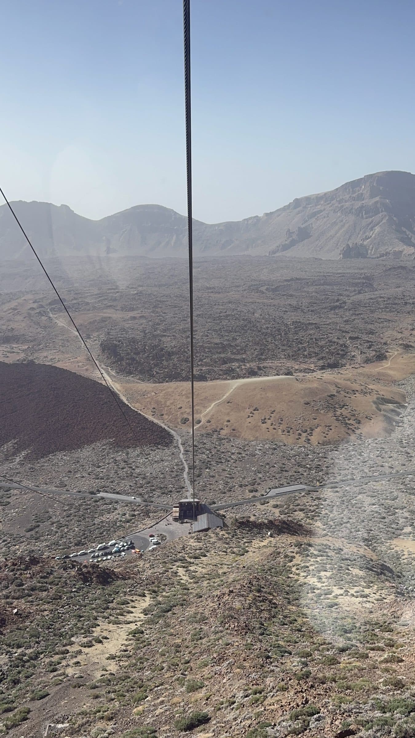 Looking down at the cable car base station and parking area from inside the ascending cabin.