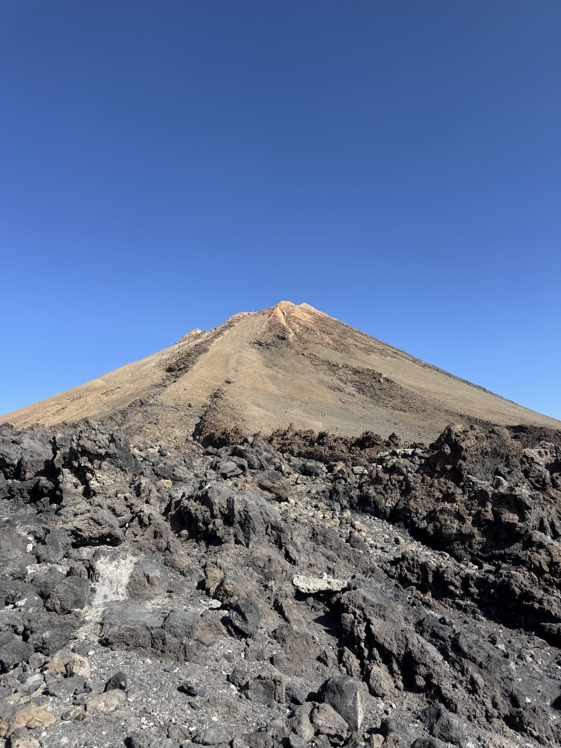 Teide's summit cone rising above the volcanic rock, seen from below against a clear sky.