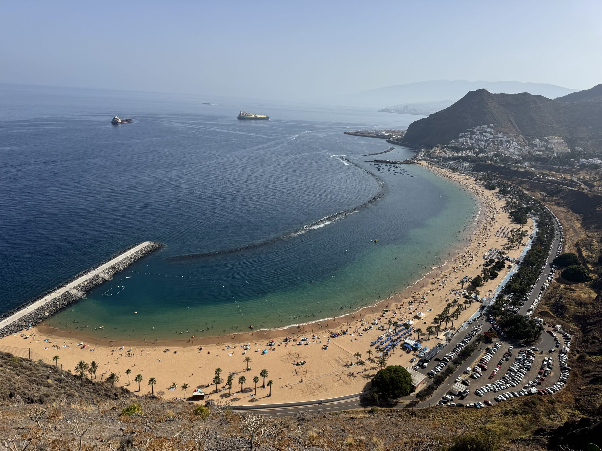 View from the Mirador de Las Teresitas over the full curve of the beach, the bay, the public parking and the hazy Santa Cruz coastline beyond.