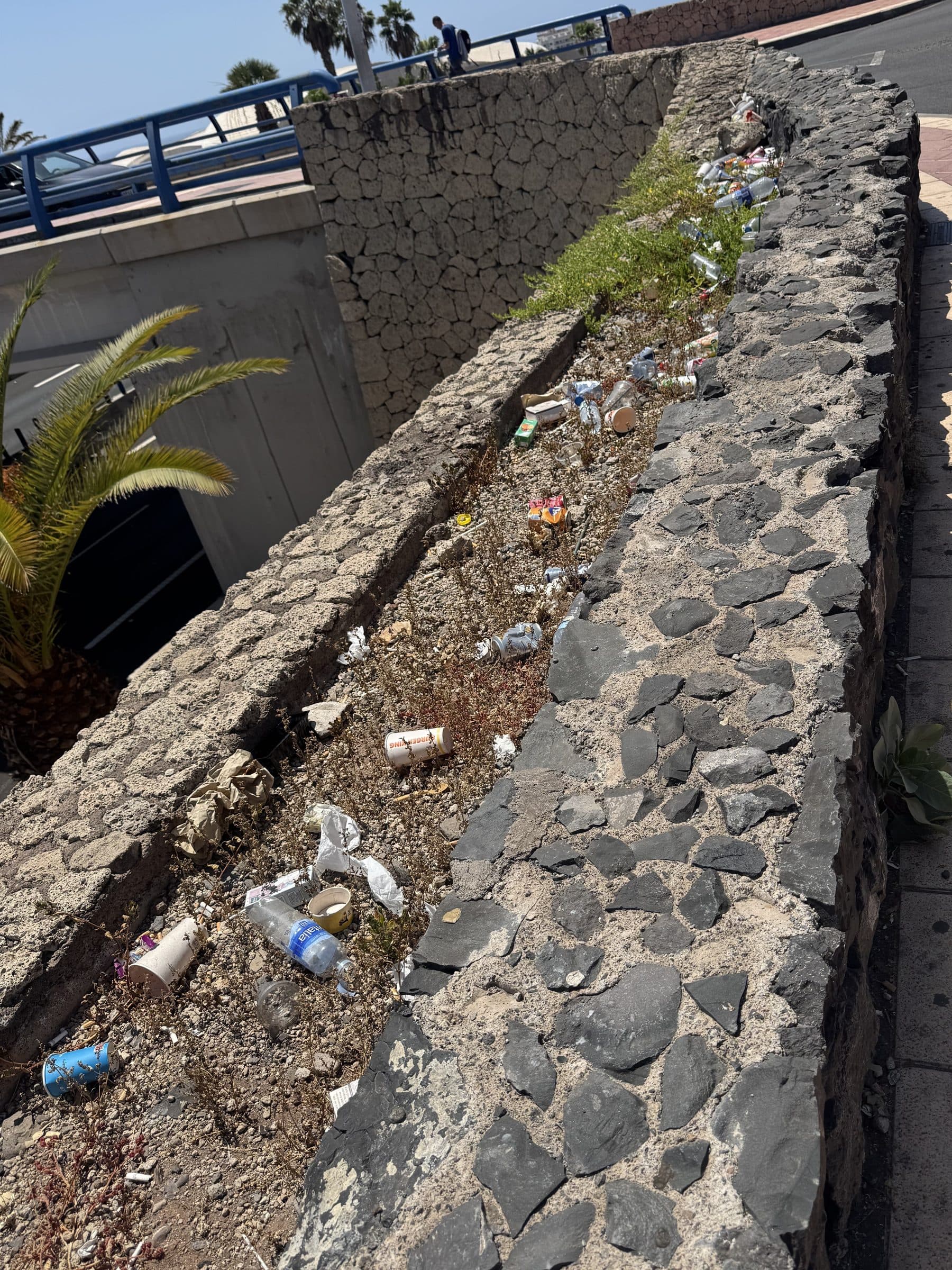 A stone roadside planter filled with discarded bottles and cans, on the walk from the car park to Siam Park.