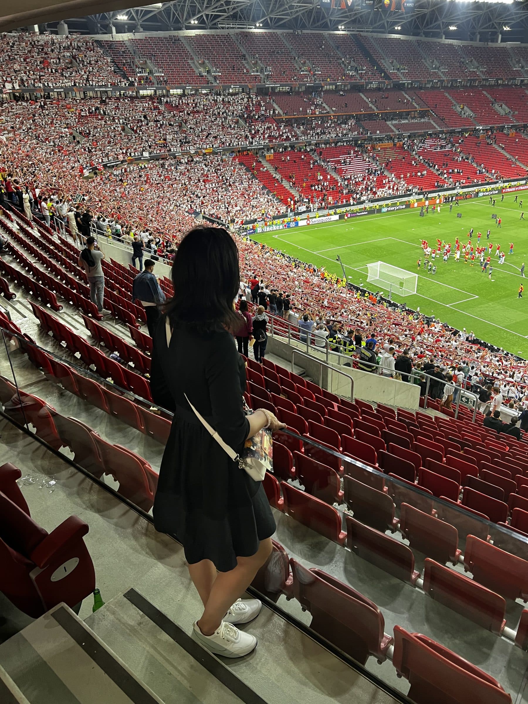 Watching a football match from the stands, photographed from behind